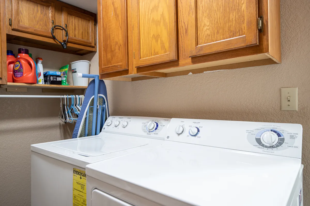 A practical interior scene focused on a modern washing machine, organized cabinets, and laundry supplies, suggesting convenient in-home amenities for guests.