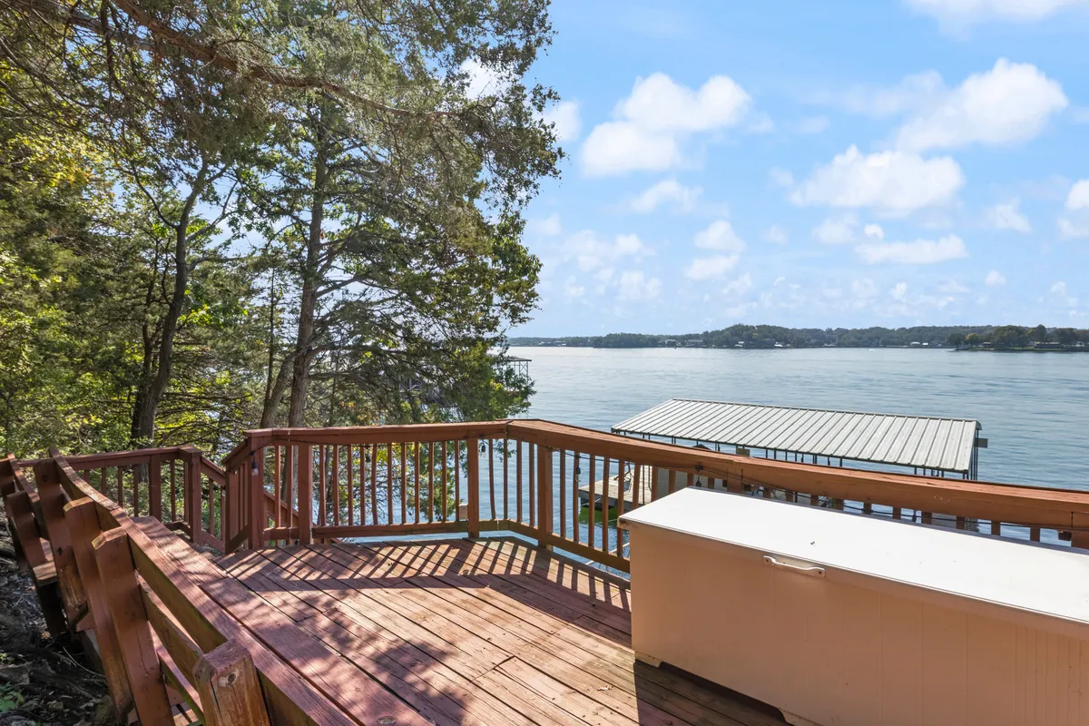 A wide deck overlooking the lake with comfortable outdoor seating and mature trees framing the view. The space is perfect for relaxing, gatherings, and enjoying sunrises or stargazing by the water.