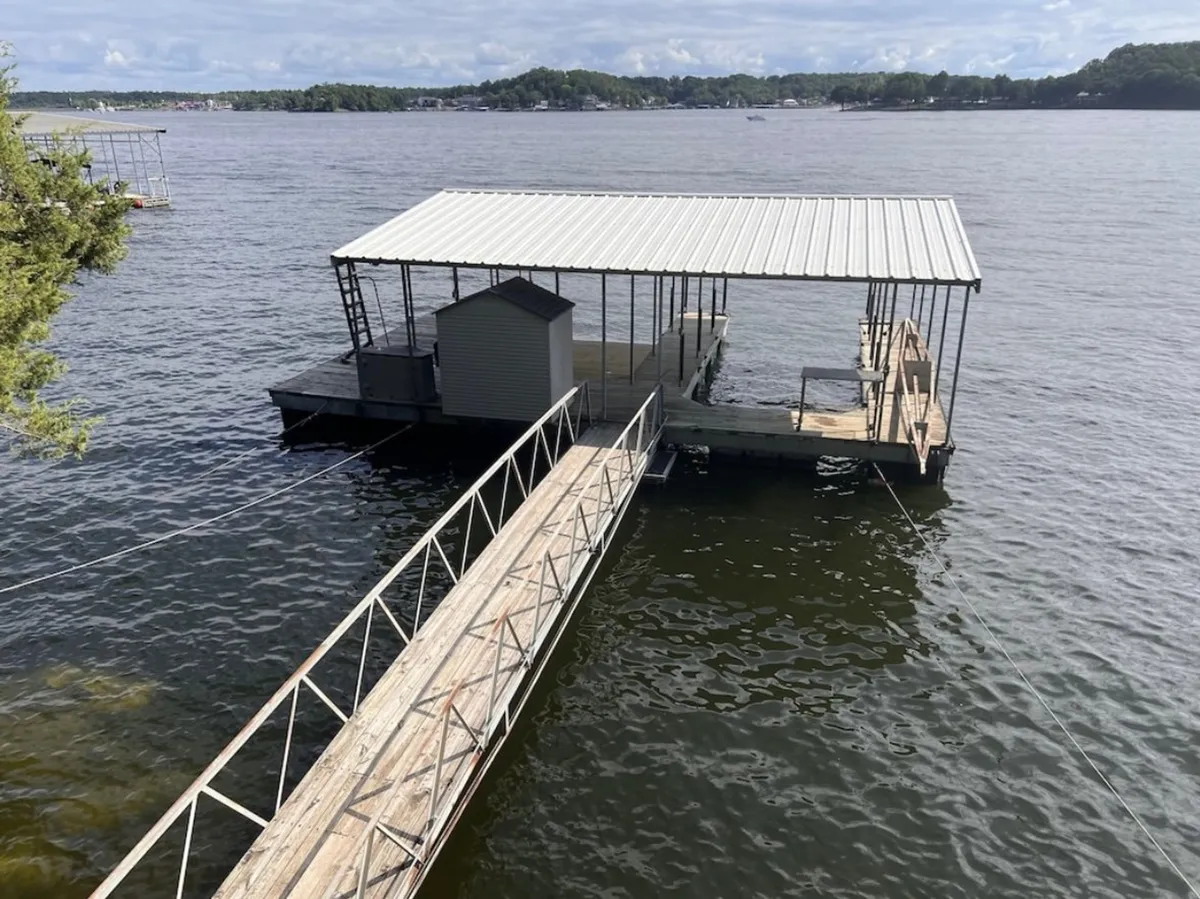 This image presents a tranquil dock scene featuring a boathouse and dock extending over calm water. The view invites boating and fishing activities, with space to relax by the water and enjoy the sunset.