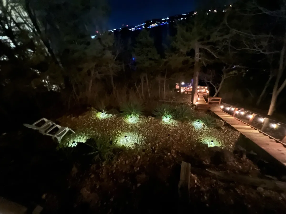 An evening exterior view of the property with illuminated garden areas and pathway lights set against natural surroundings. The scene is tranquil, suggesting a well-cared-for and secure environment, especially at night.
