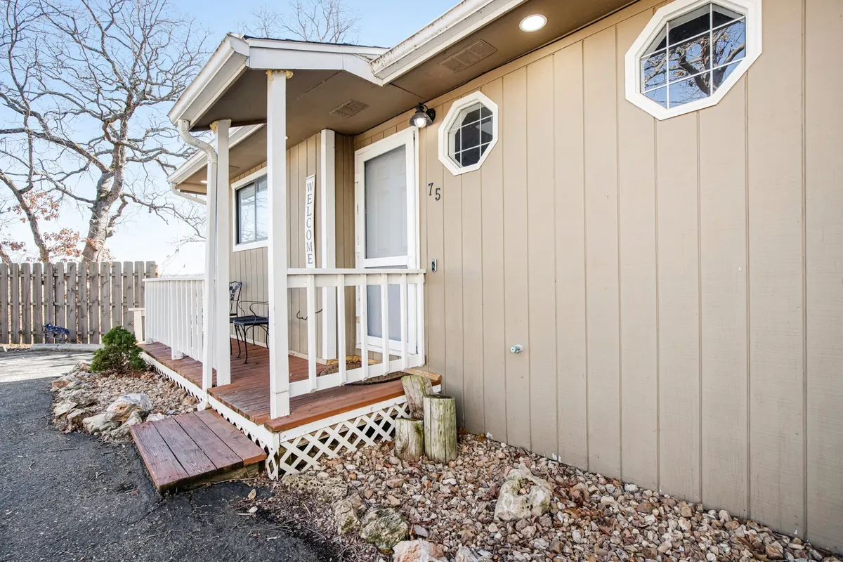 The front porch of the property features a welcome sign, octagonal windows, and a wooden deck surrounded by trees. The space is inviting, with comfortable seating and a design that encourages guests to relax outside and enjoy the peaceful environment before heading out to explore.