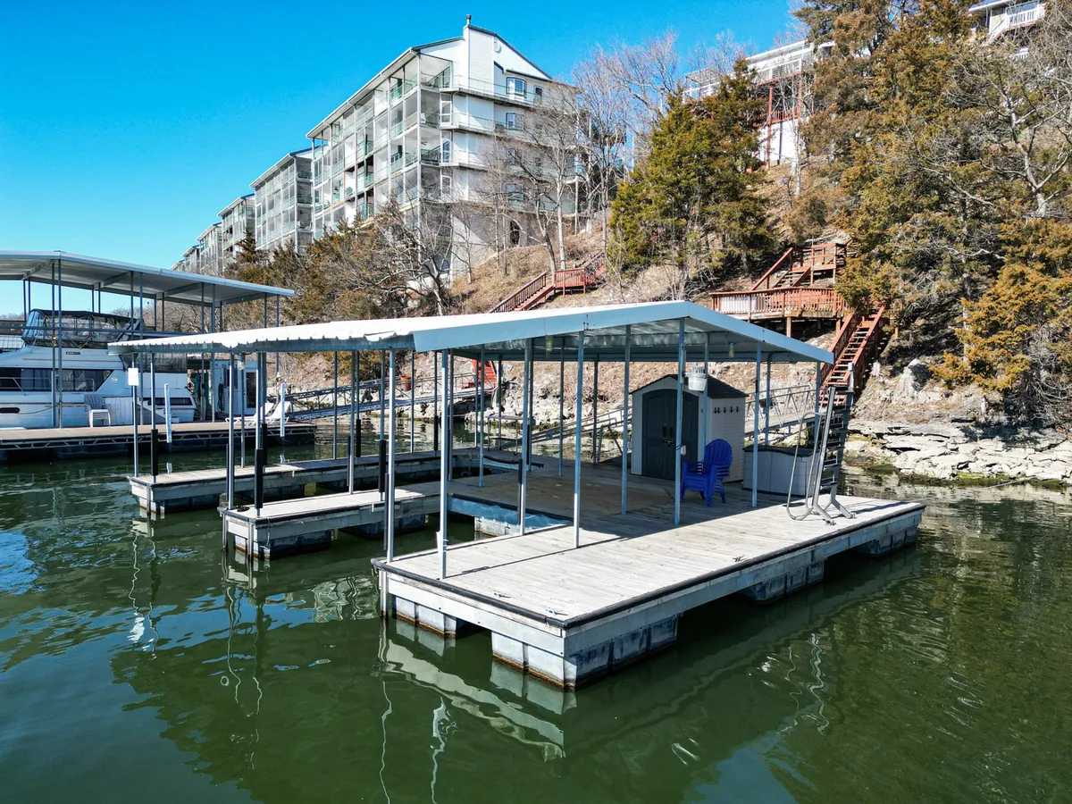 A serene lakeside scene featuring a boathouse and docks surrounded by lush trees. The water is calm and inviting, ideal for fishing or simply soaking up the lakefront ambiance. The natural beauty and quiet of this area are showcased.